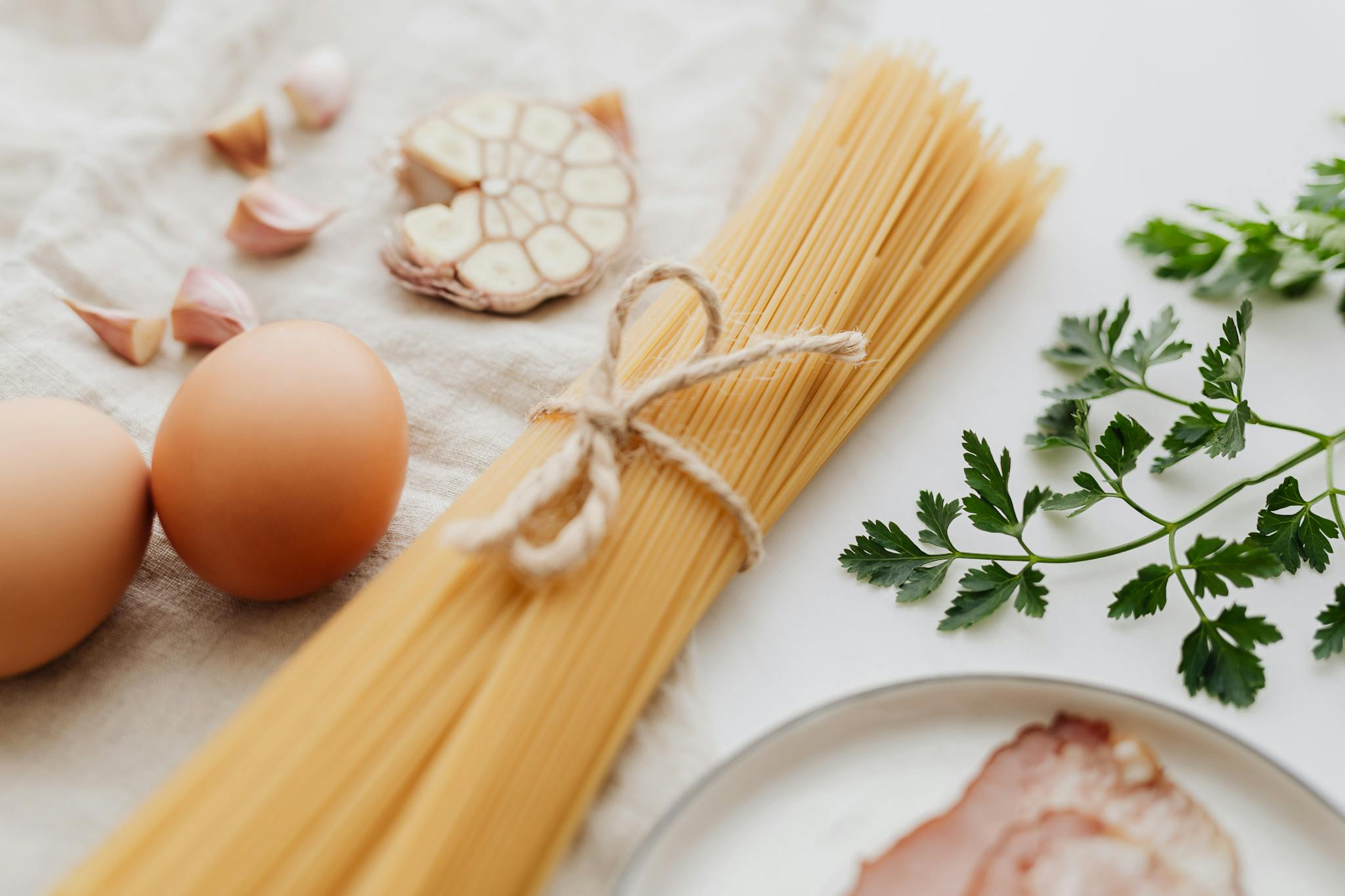 A flat lay of fresh ingredients including spaghetti, eggs, garlic, and parsley for a delicious pasta dish.