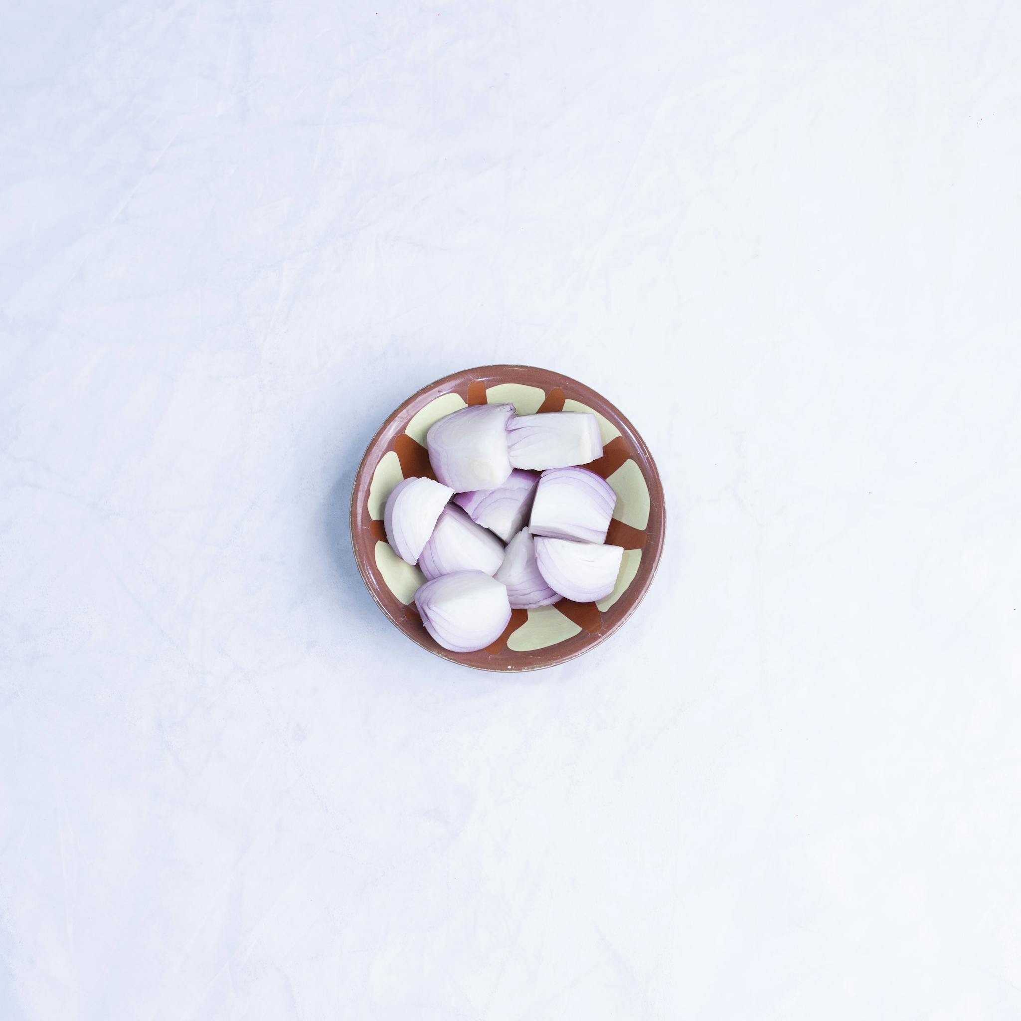 A flat lay of fresh onion pieces in a decorative bowl on a white marble surface.