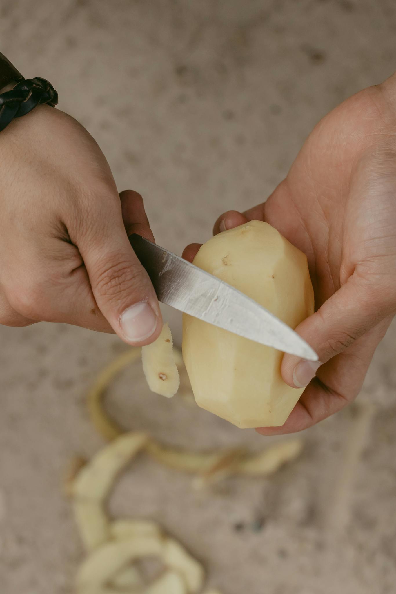 Detailed view of a person peeling a potato using a knife, showcasing culinary preparation skills.