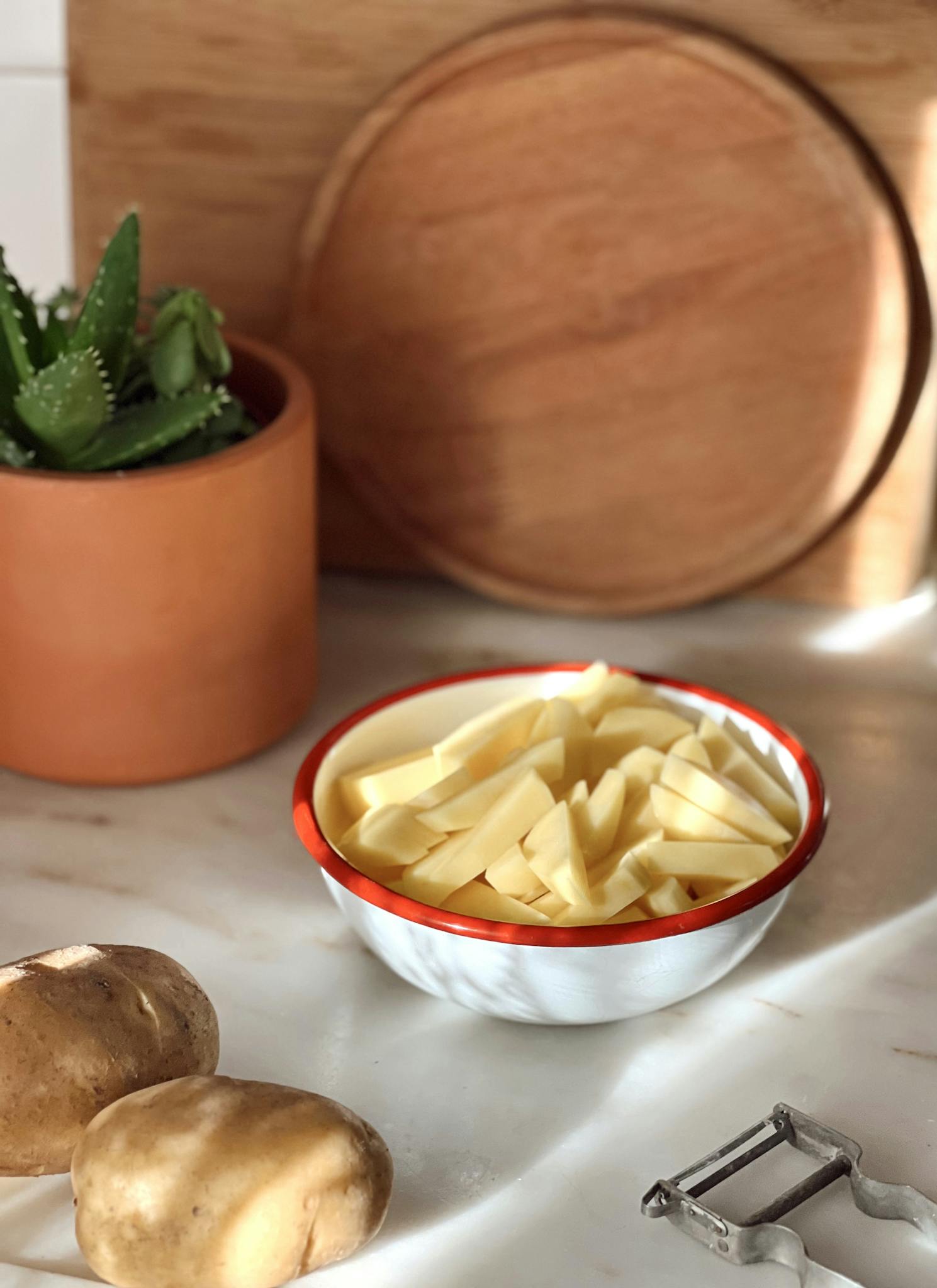 Sliced potatoes ready for cooking in a rustic kitchen setting with natural light.