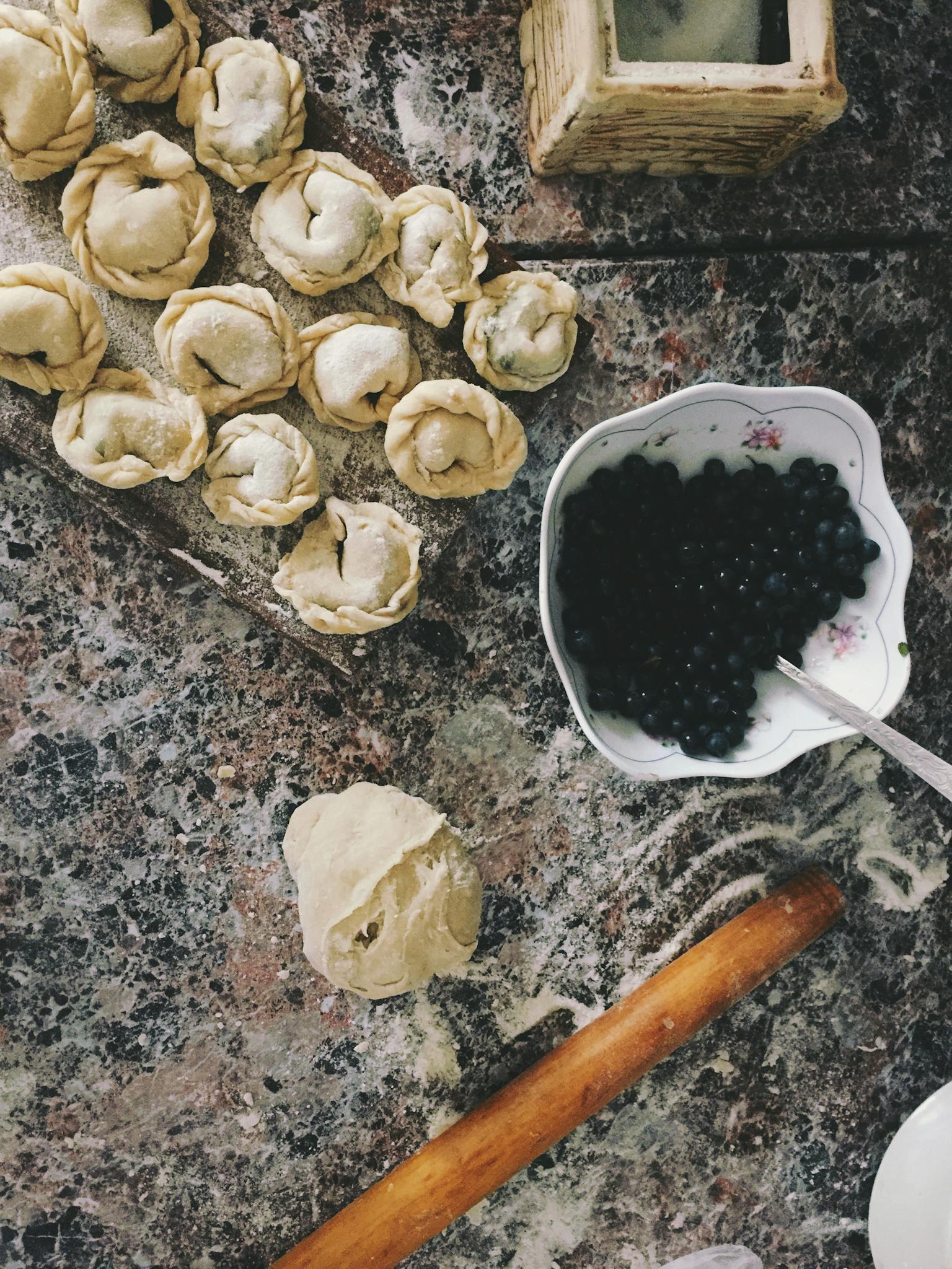 Top view of dough, blueberries and a rolling pin on a marble surface for homemade pastries.